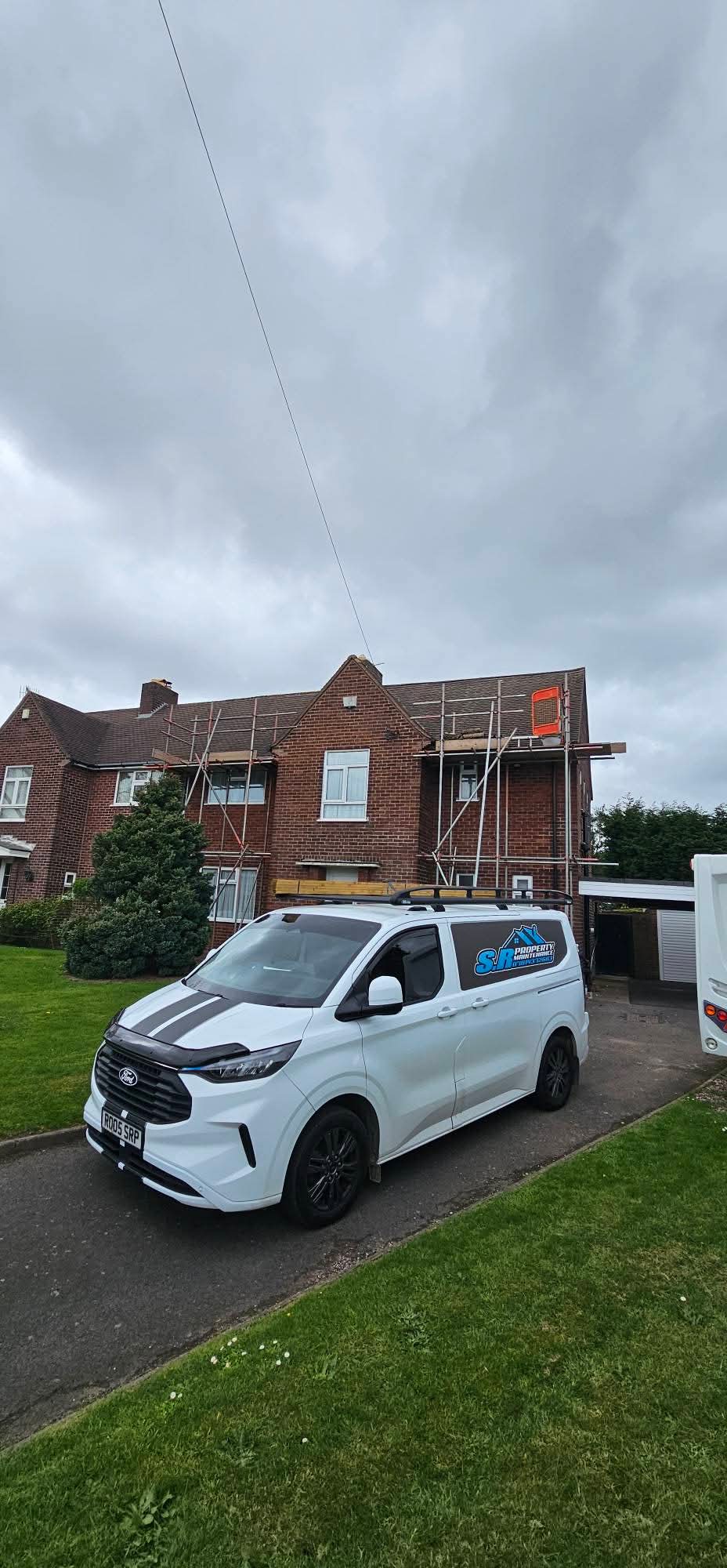 S R Property Maintenance van outside a scaffolded semi-detached house with roofing materials on the van roof rack